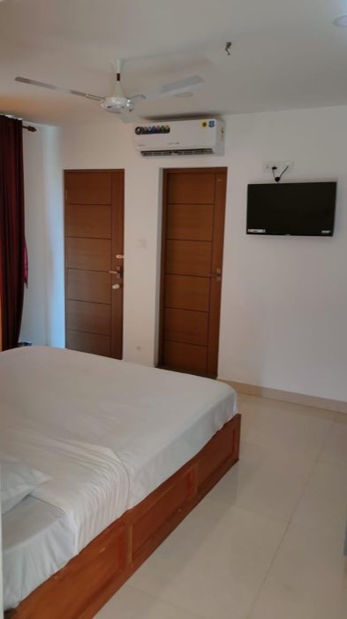 A standard room at Vanyora with a double bed, wall-mounted air conditioner, television and teak doors.
