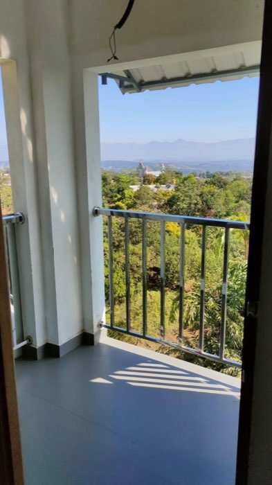 The view from a Vanyora balcony over treetops towards a hilltop church and a long line of blue mountains.